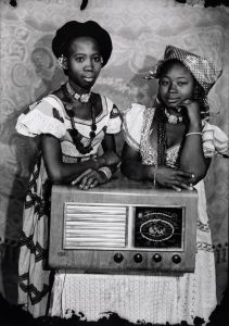 Black and white photo of two young women standing next to a vintage radio.